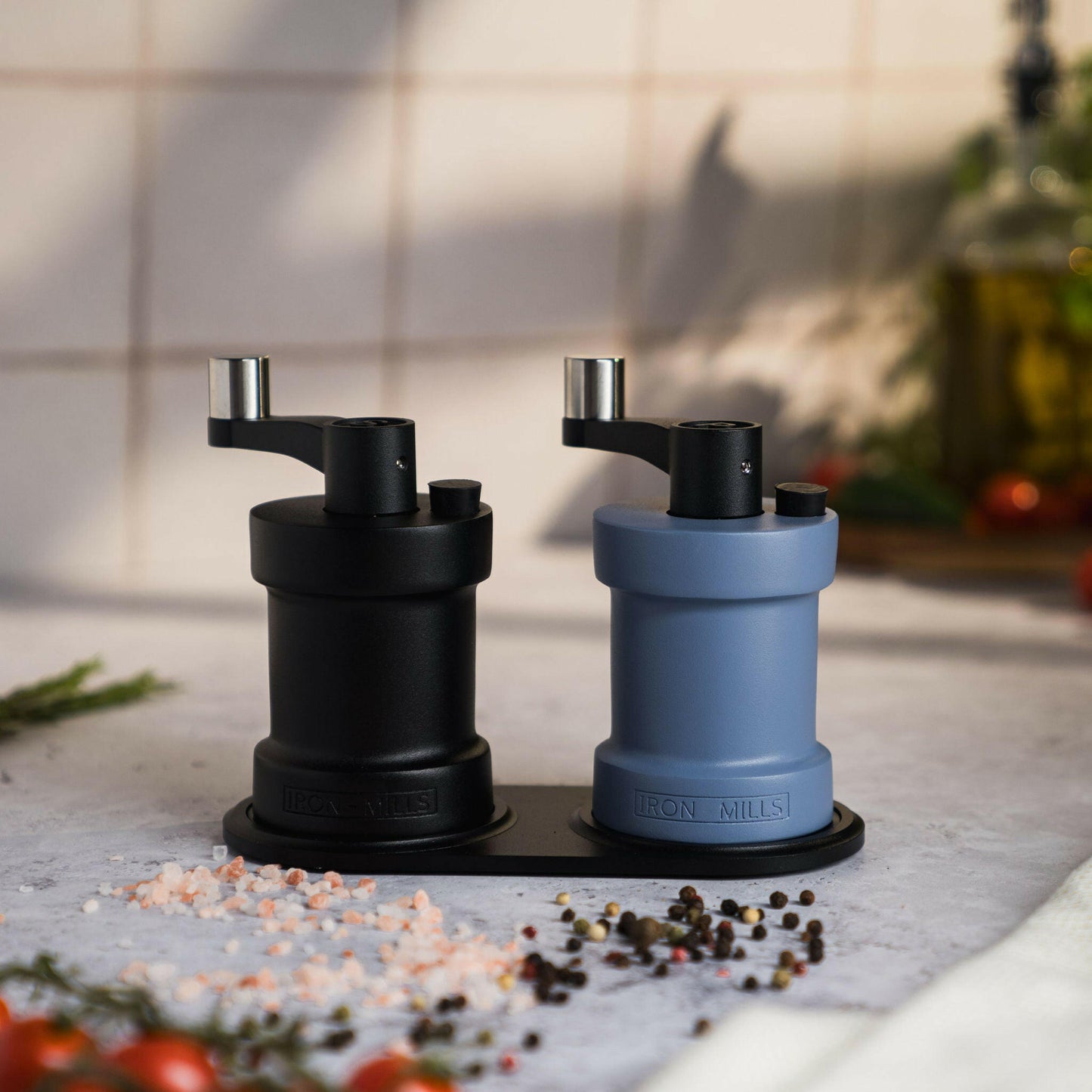 Iron-Mills onyx black and pigeon blue salt and pepper mills resting on a sleek mill base in a bright kitchen arrangement