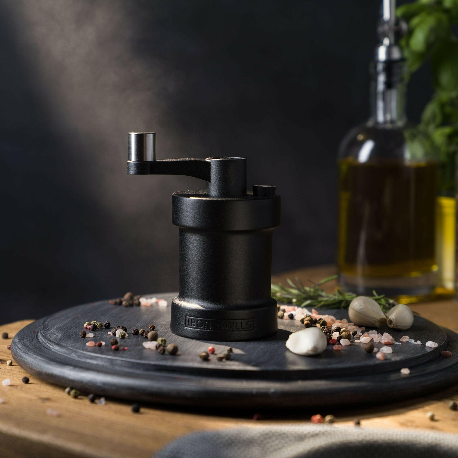 Iron-Mills onyx black salt mill on a chopping board in a bold modern kitchen with peppercorns nearby